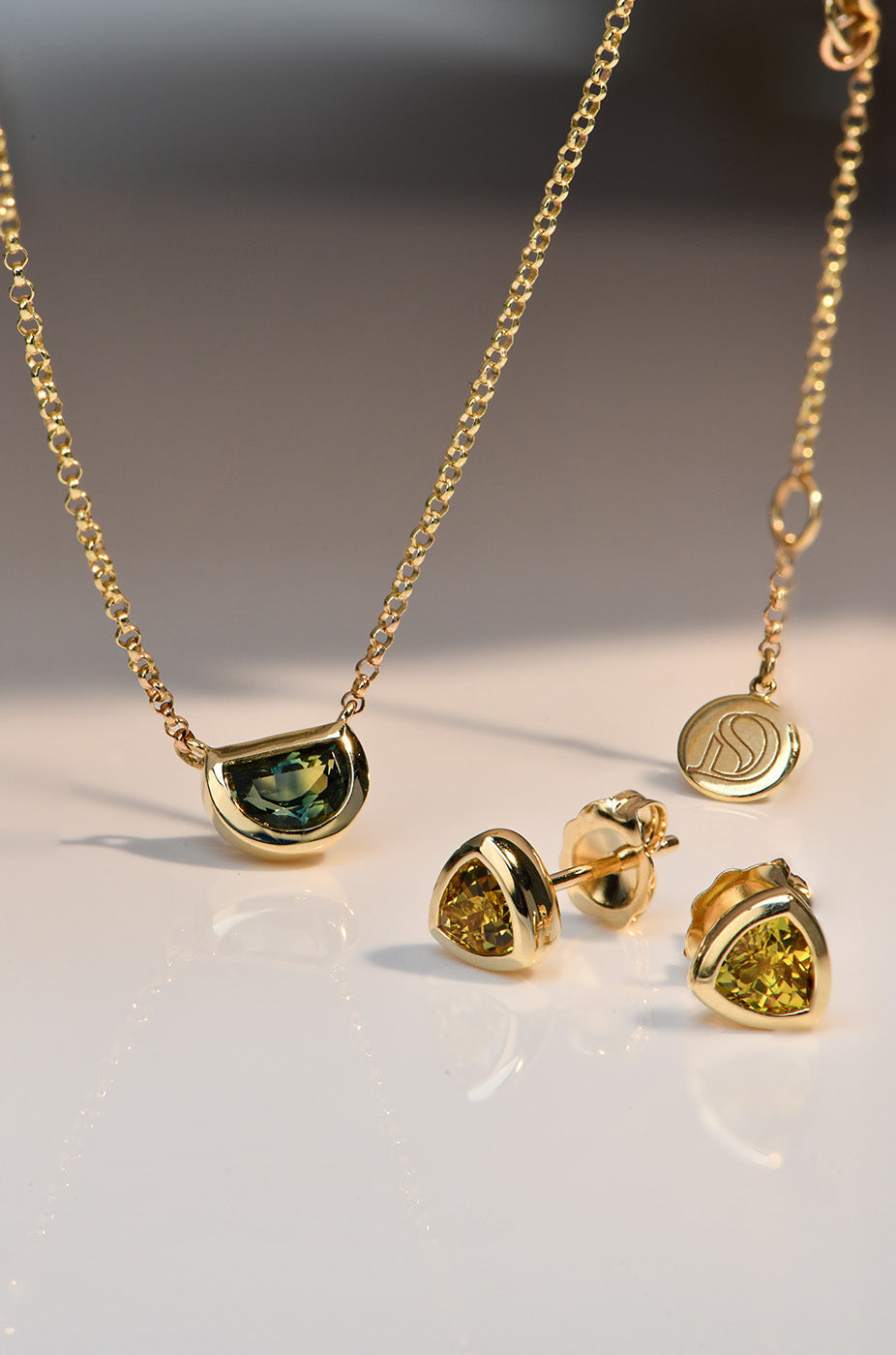 Gold necklace and earrings with green and yellow Australian Sapphires on a light background